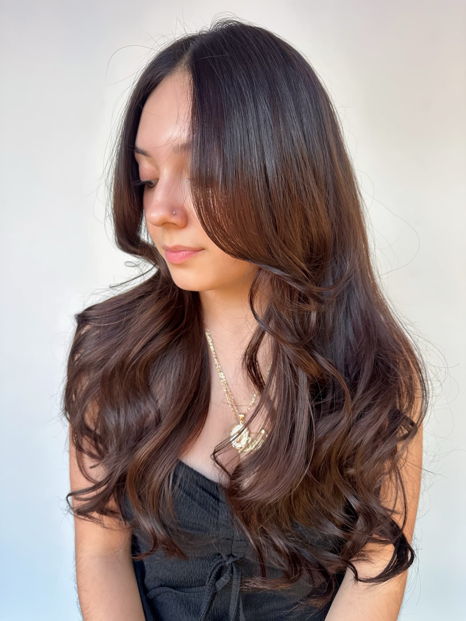 Long chocolate-brown layers with face-framing pieces falling forward, cut to move with the hair's natural wave