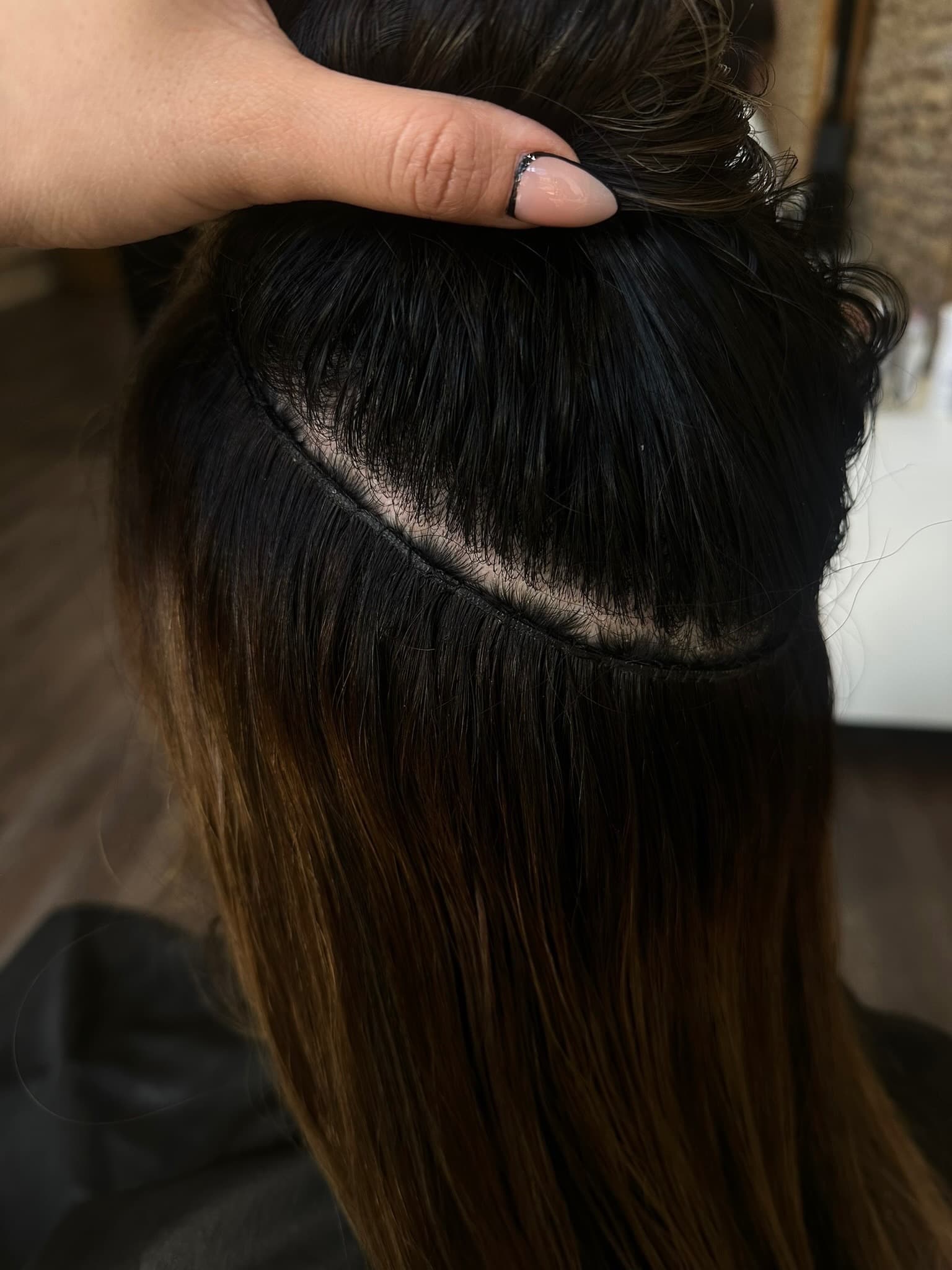 Close-up of a hand-tied weft lifted to show extensions blended invisibly into natural hair